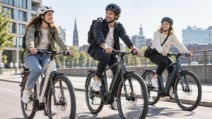 Drei junge Erwachsene fahren mit Helmen auf modernen Urban-E-Bikes durch eine helle europäische Stadt.