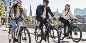 E-Bikes werden bei jungen Erwachsenen deutlich beliebter – das steckt dahinter Drei junge Erwachsene fahren mit Helmen auf modernen Urban-E-Bikes durch eine helle europäische Stadt.